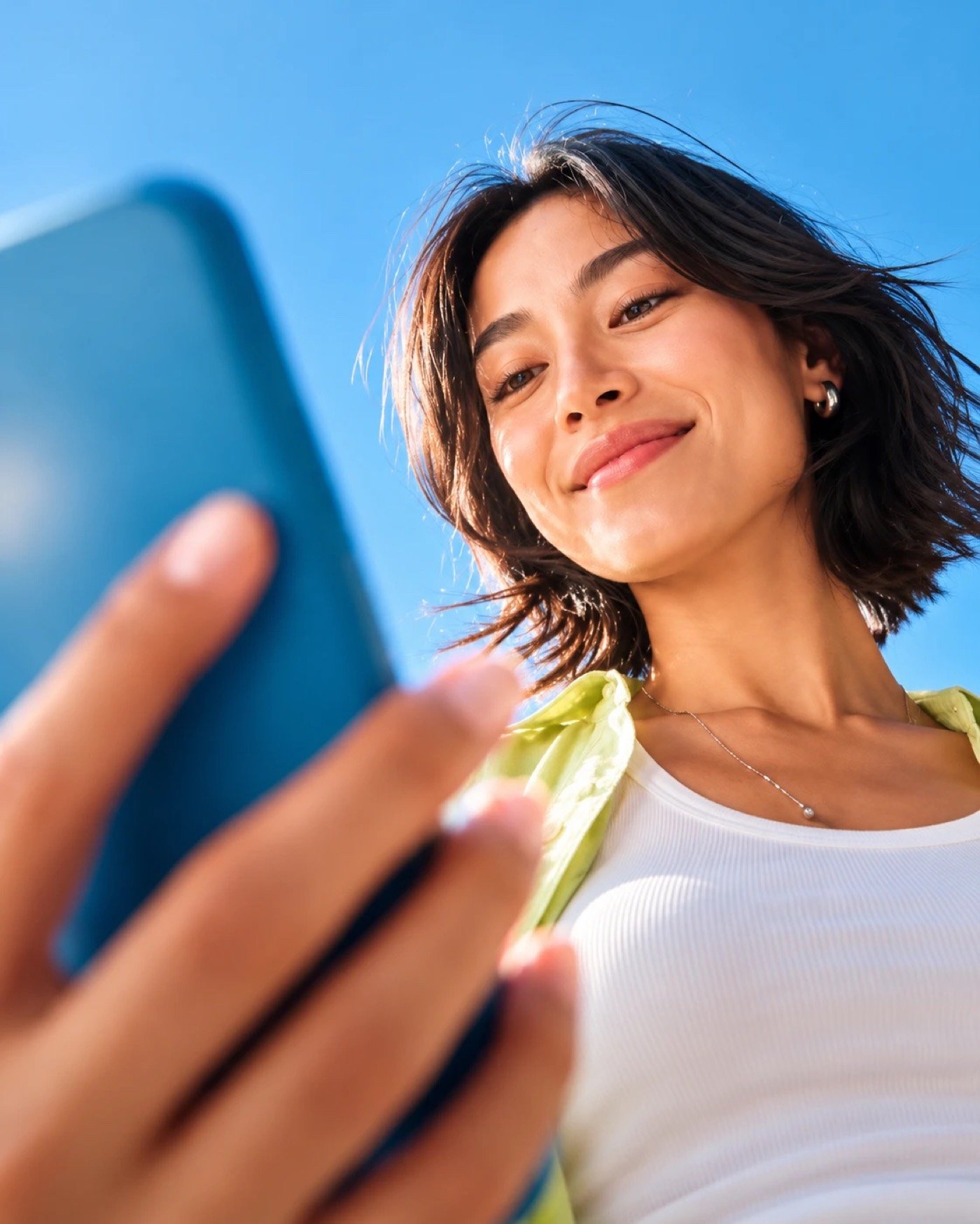 Smiling woman checking her phone under a clear blue sky